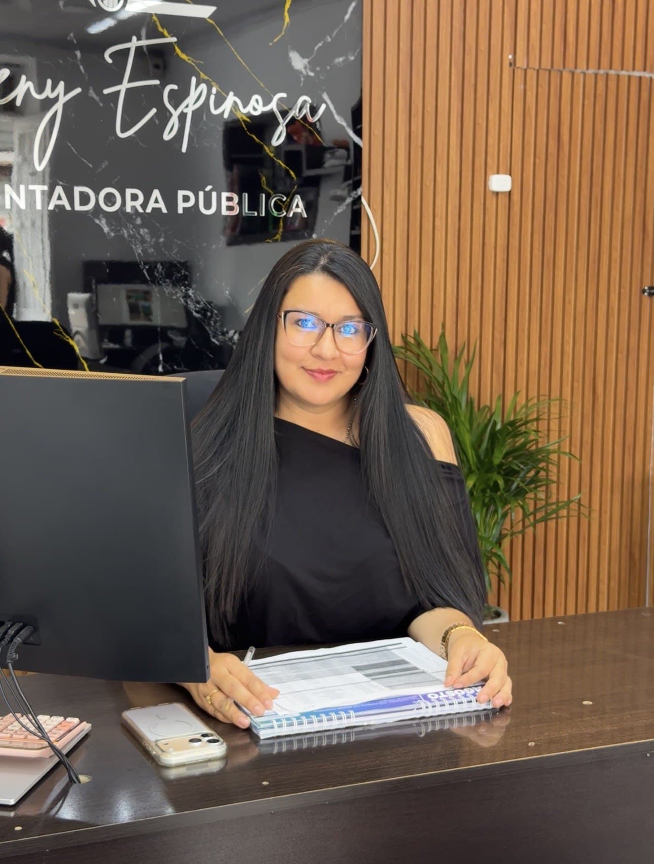 Yeny Espinosa sonriendo en su escritorio, frente al letrero de su oficina